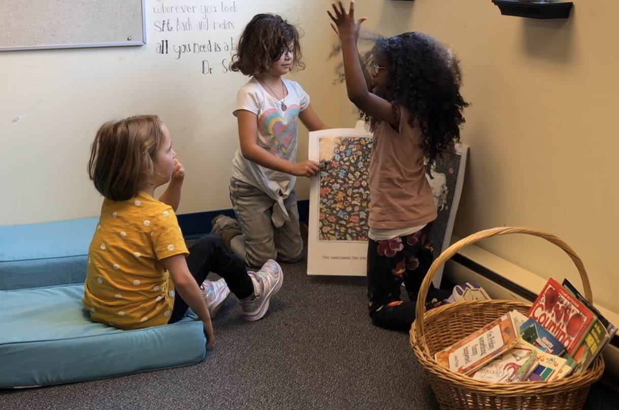 a student reads a big book to two other students